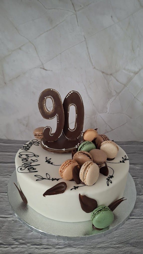 Weiße Geburtstagstorte mit Macarons, Schokoladenzahl 90 und Happy-Birthday-Schriftzug